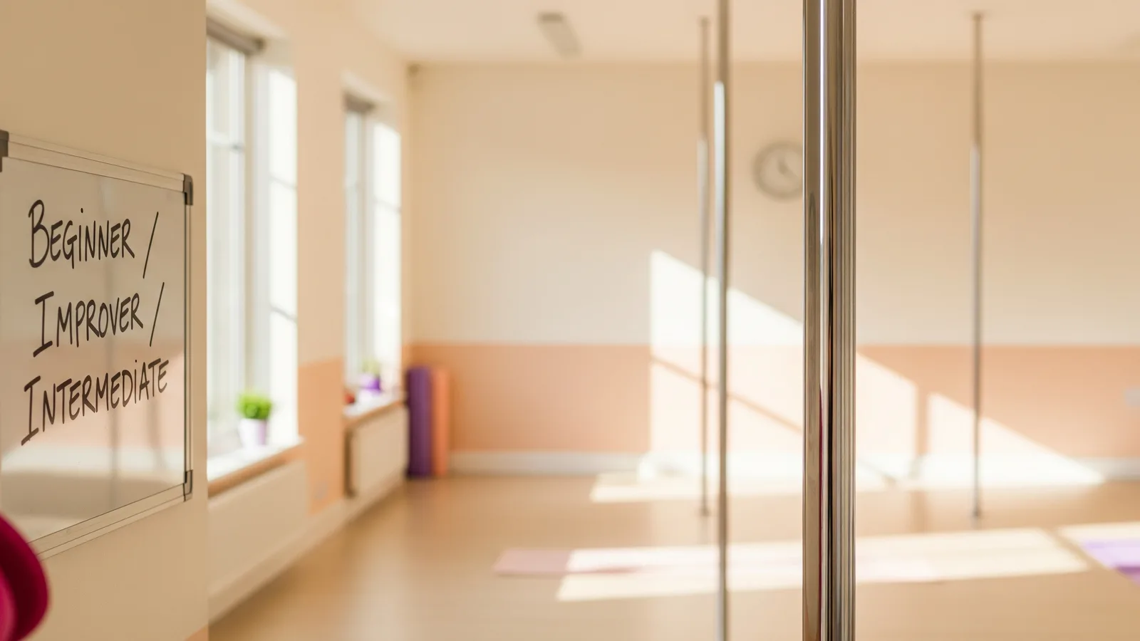 A chrome pole against a warm studio wall beside a small whiteboard listing class levels